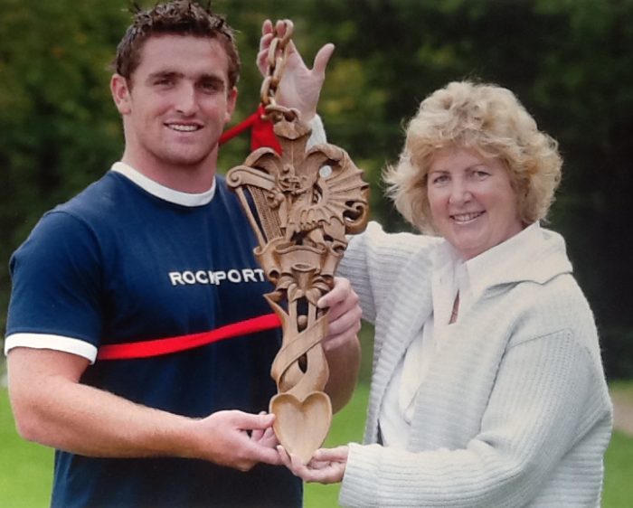 Huw Bennett receiving the Team's new mascot from The Lovespoon Gallery of Mumbles in 2003.  He was the youngest member of the team at the time and this has continued to be the Team tradition ever since.  